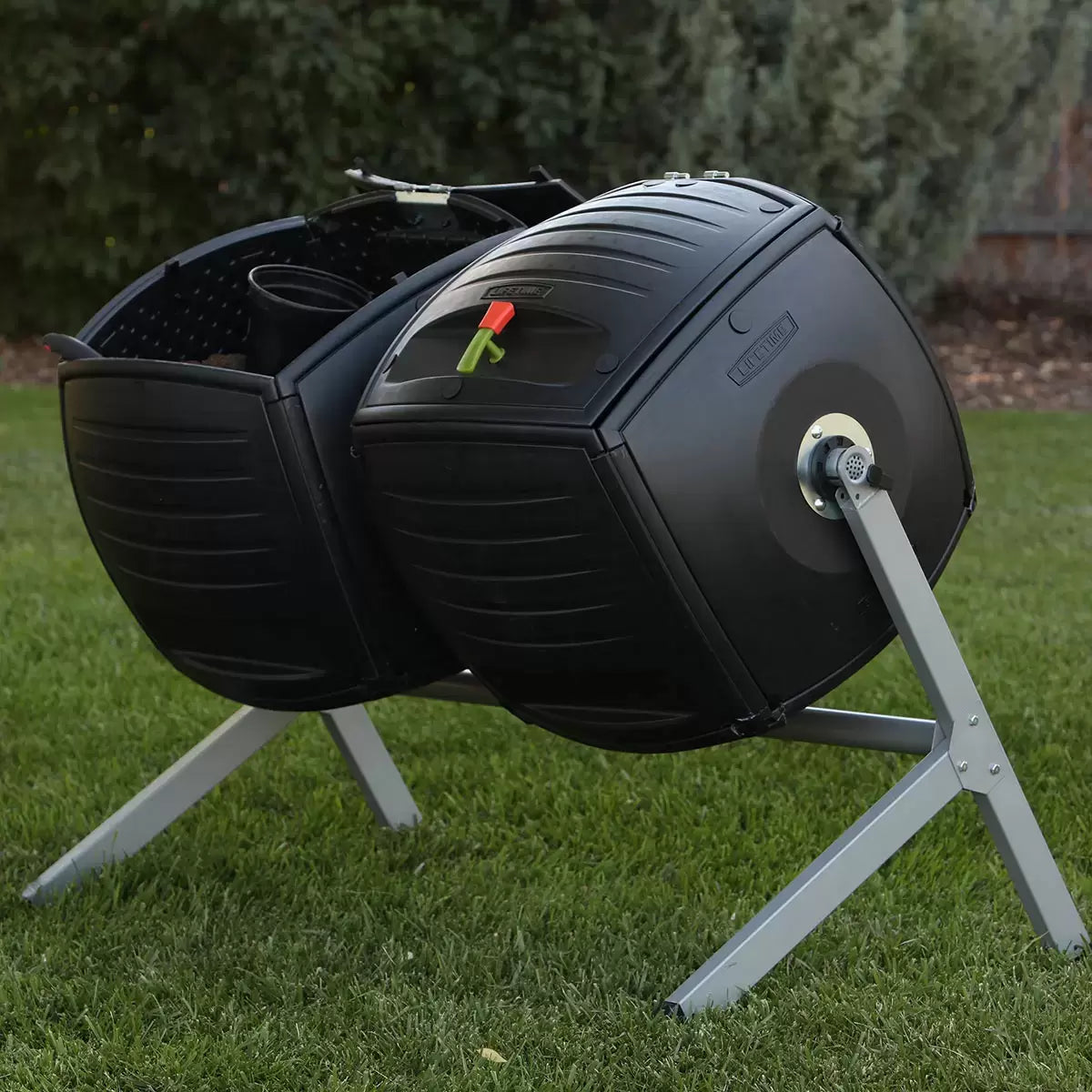 A side-by-side view of the Lifetime 378L dual tumbling composter on a sturdy steel base, situated on a clean garden patio, showing the black panels and red processing indicators.