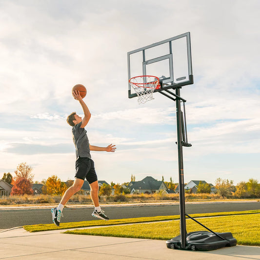 Front three-quarter view of the Lifetime 52 inch shatterproof basketball hoop system with black steel pole and portable base set up on an outdoor driveway.