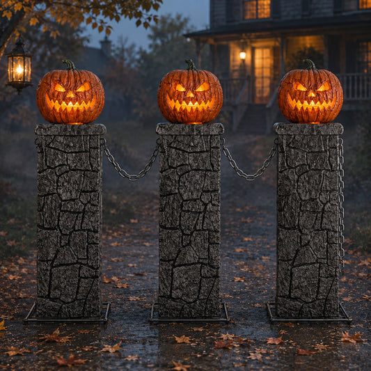 Three grey gothic stone pedestals with orange lit LED jack-o'-lantern tops connected by black chains on a dark outdoor lawn.