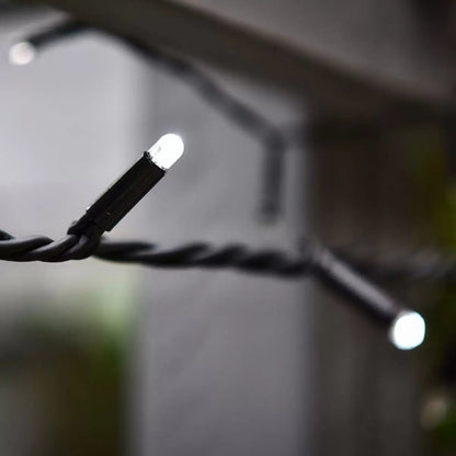 Close-up of bright ice white LED bulbs on a dark green rubber cable strung across a dark outdoor patio garden at night.