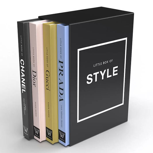 Four pocket-sized hardback fashion books featuring Chanel, Dior, Gucci, and Prada resting inside a black slipcase on a white wooden surface.