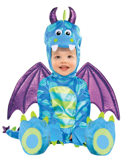 Front angle of a toddler wearing a green and yellow spotty plush Little Dragon jumpsuit with soft claws, attached tail, wings, and padded horned hood in a wooden nursery room.
