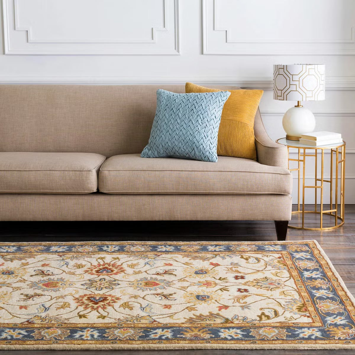 Top-down angle showing the detailed cream and muted floral pattern of the hand-tufted Livabliss Caesar wool rug styled on light oak flooring under a wooden coffee table.