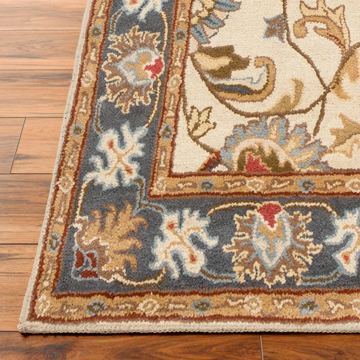 Top-down angle showing the detailed cream and muted floral pattern of the hand-tufted Livabliss Caesar wool rug styled on light oak flooring under a wooden coffee table.