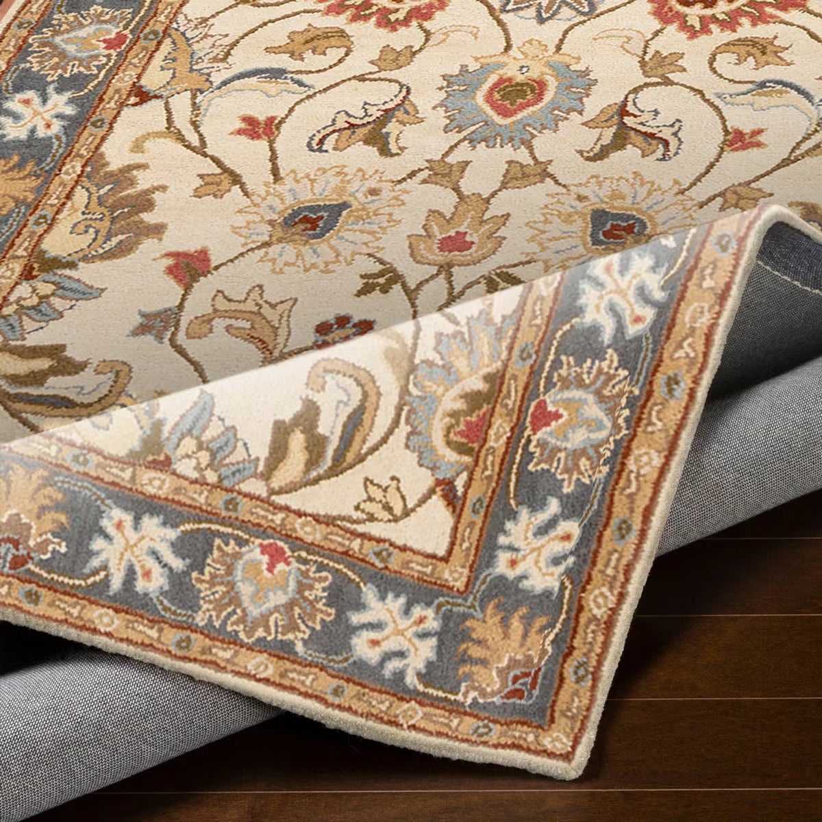 Top-down angle showing the detailed cream and muted floral pattern of the hand-tufted Livabliss Caesar wool rug styled on light oak flooring under a wooden coffee table.