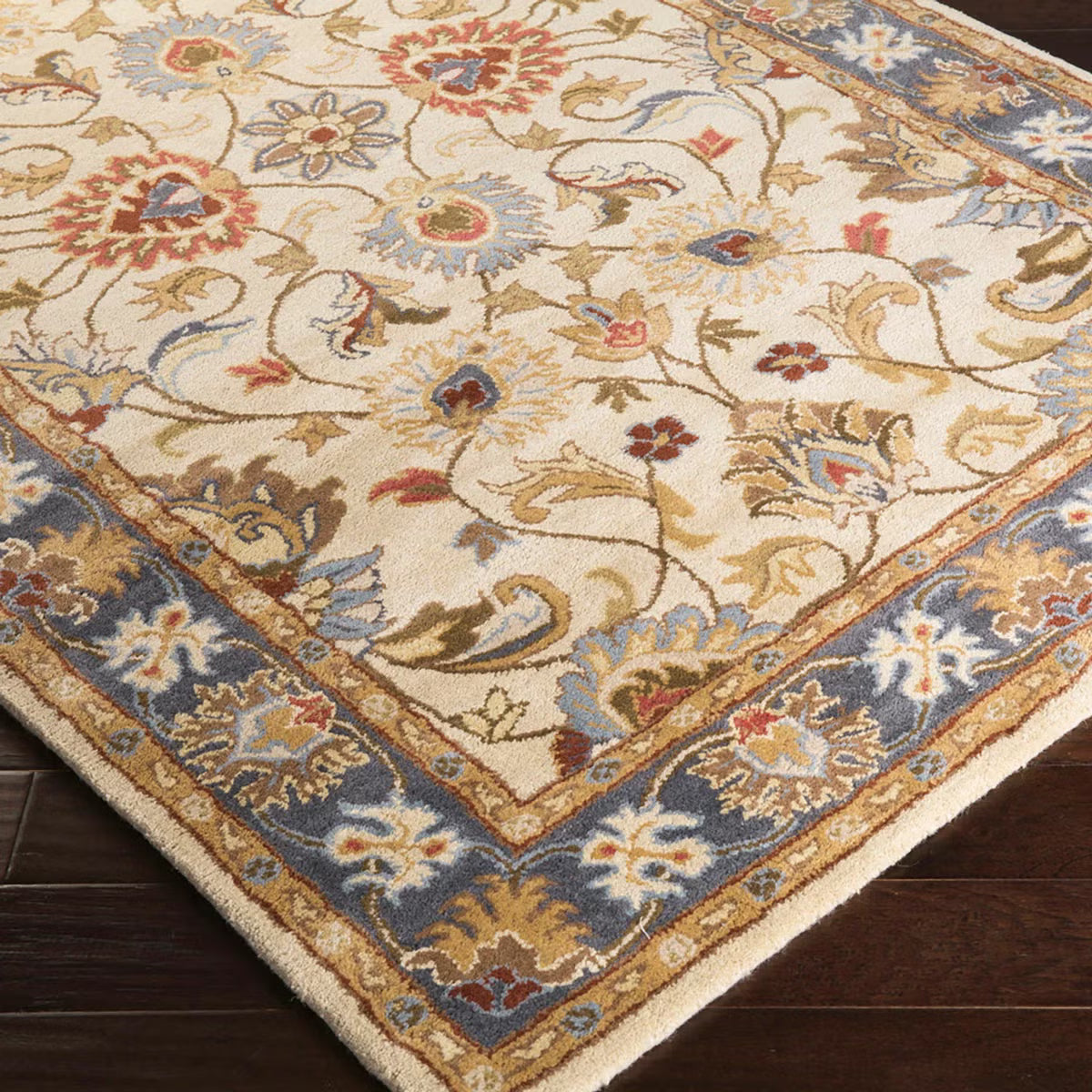 Top-down angle showing the detailed cream and muted floral pattern of the hand-tufted Livabliss Caesar wool rug styled on light oak flooring under a wooden coffee table.