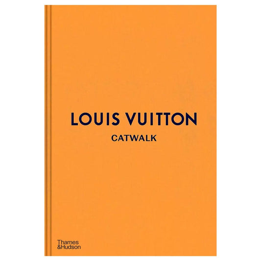Opened hardcover book Louis Vuitton Catwalk displaying vibrant runway photographs and text on a dark wooden surface.
