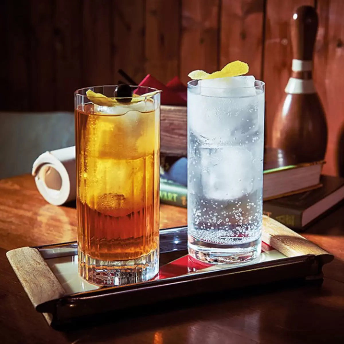 Eight Luigi Bormioli Bach hi-ball glasses arranged on a sleek marble bar top, showcasing their tall, fluted, and faceted crystal design.