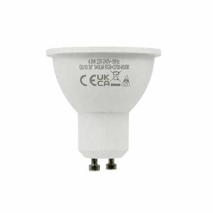 Four white Luminus Smart GU10 LED spotlight bulbs arranged neatly on a dark wooden countertop casting a soft multi-coloured glow.