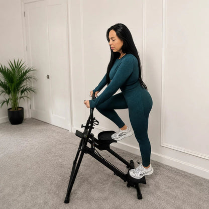 Front angle view of the black MAXhealth Climb Stair Climber with adjustable handles, foot pedals, and digital screen set up in a modern living space.