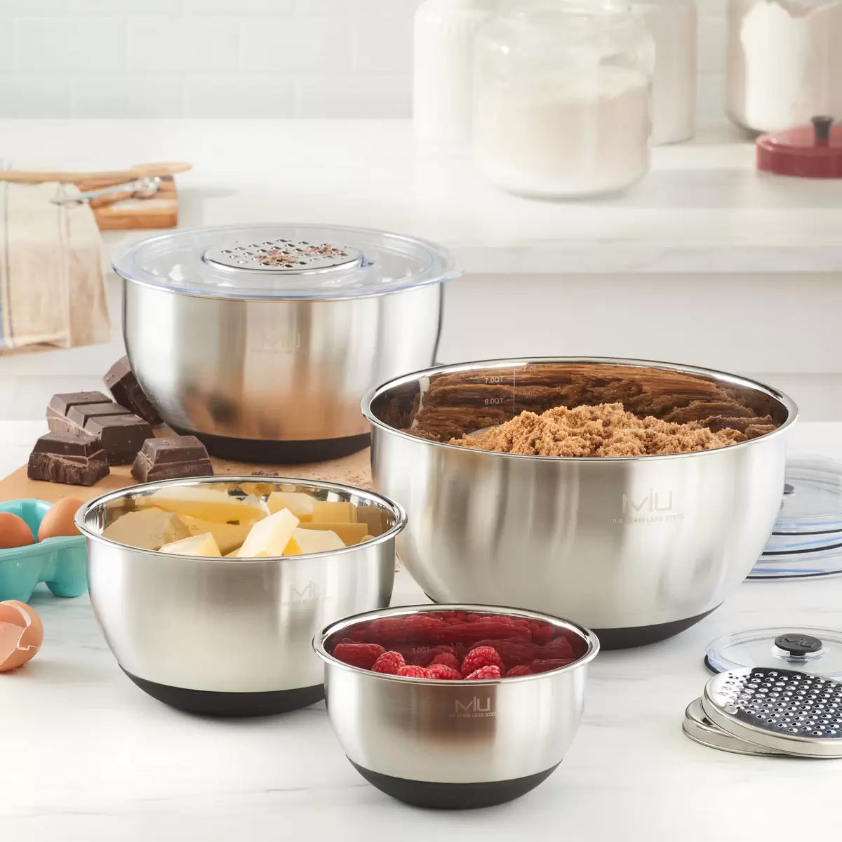 Full 11-piece MIU stainless steel mixing bowl set with graters and lids arranged on a kitchen counter.