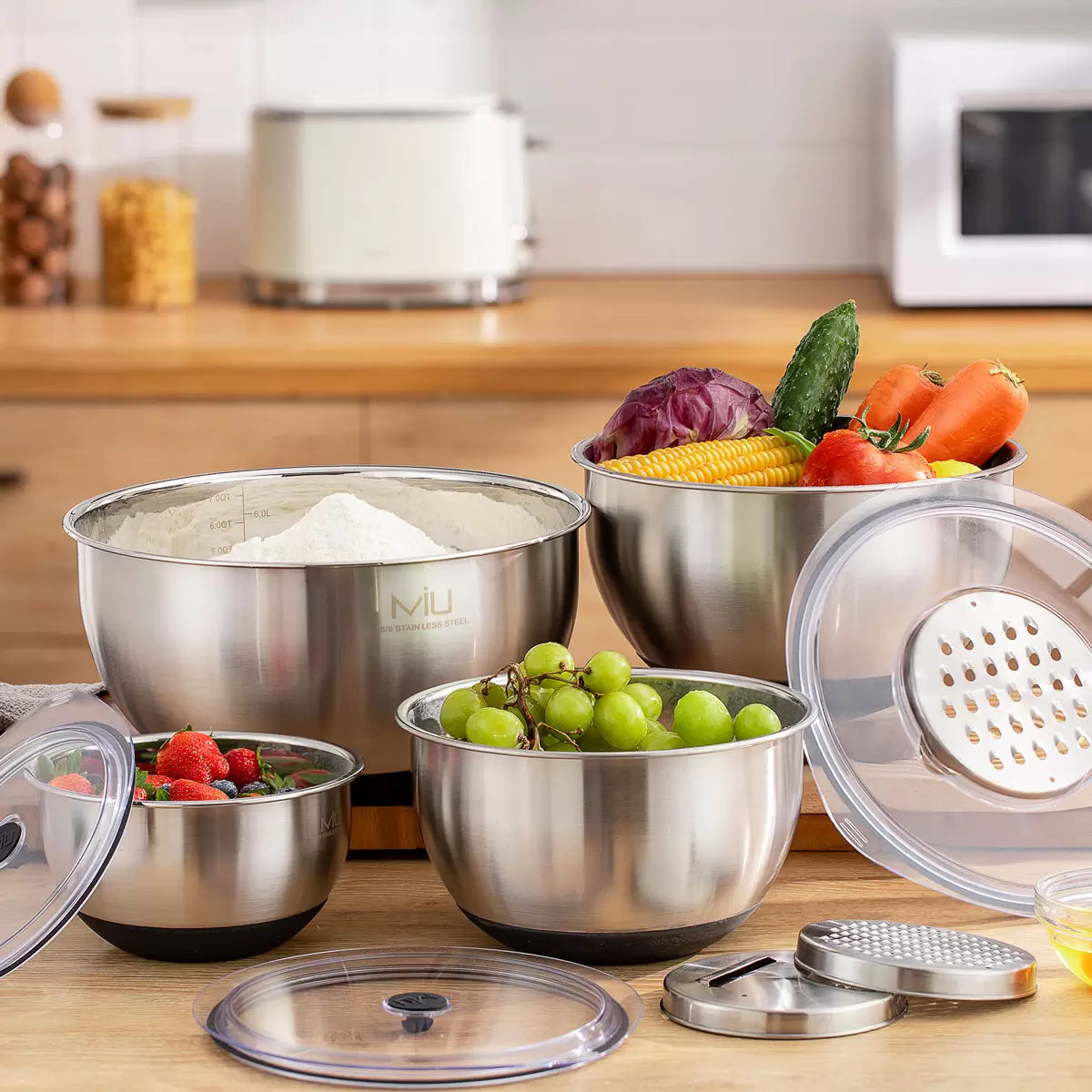 Full 11-piece MIU stainless steel mixing bowl set with graters and lids arranged on a kitchen counter.