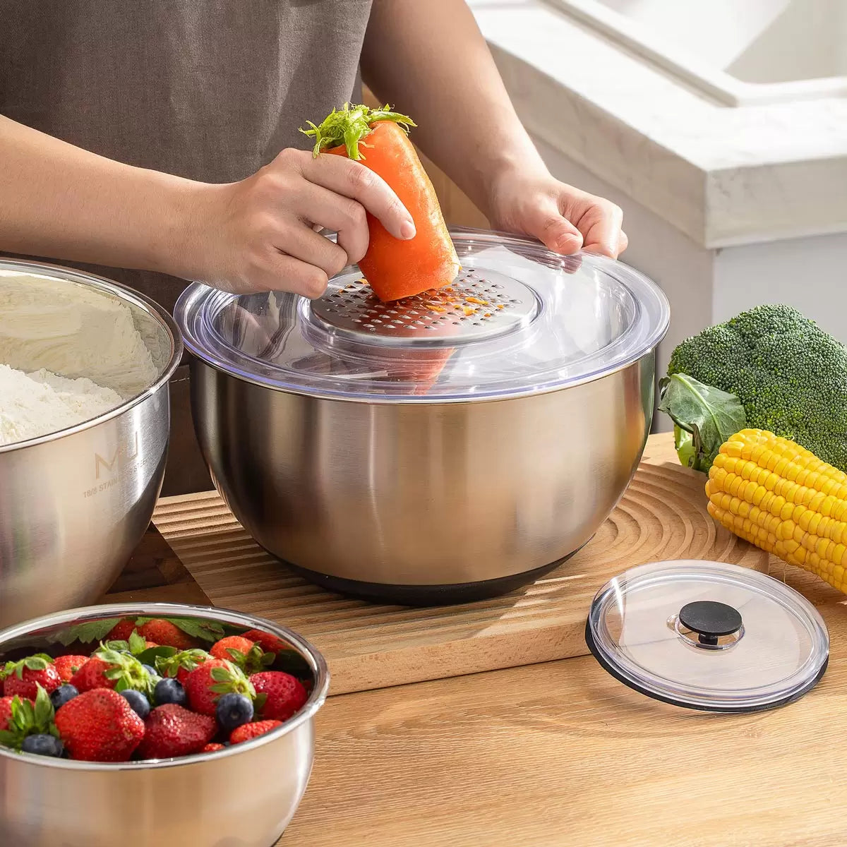 Full 11-piece MIU stainless steel mixing bowl set with graters and lids arranged on a kitchen counter.