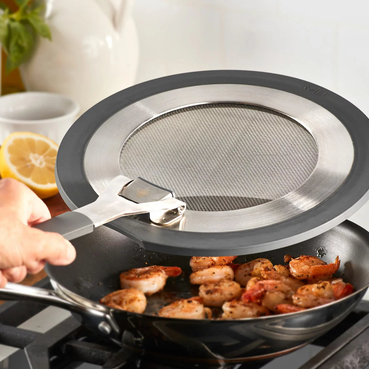 MIU 2-piece stainless steel splatter screen set with foldable silicone handles displayed next to frying pans.