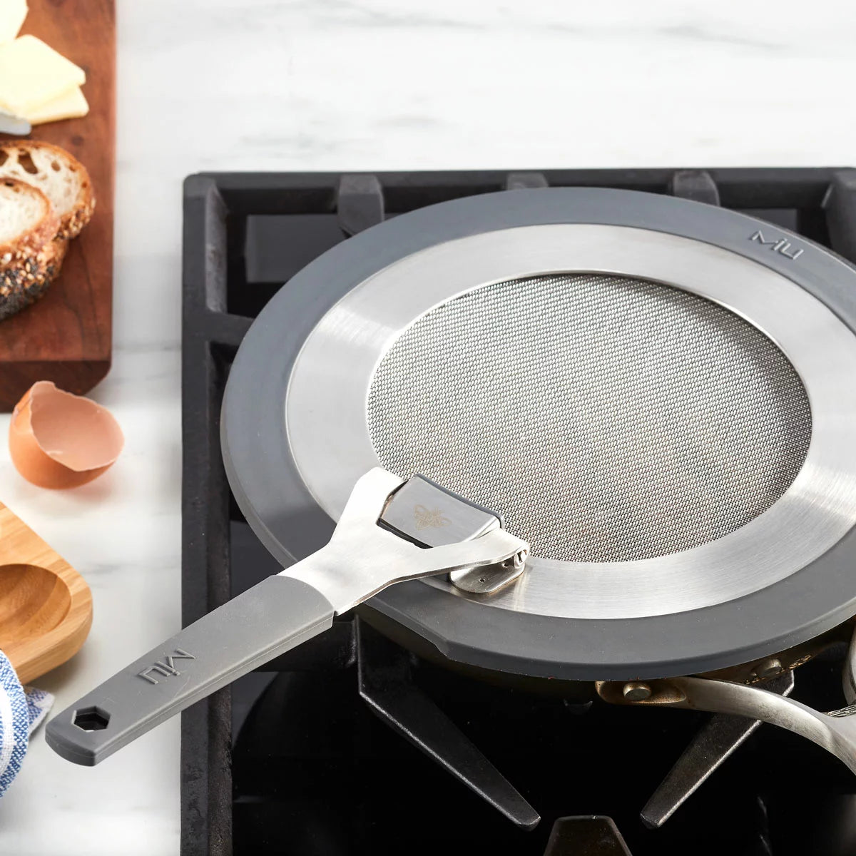 MIU 2-piece stainless steel splatter screen set with foldable silicone handles displayed next to frying pans.