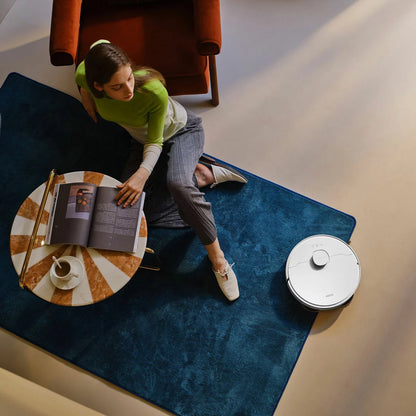 Top-down view of the sleek white MOVA E30 Ultra Robot Vacuum docking into its tall auto-empty cleaning station on light hardwood flooring.