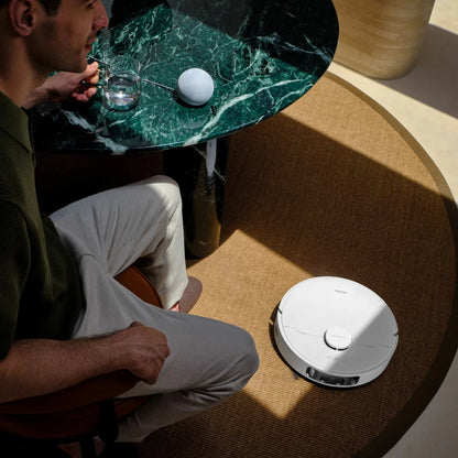 Top-down view of the sleek white MOVA E30 Ultra Robot Vacuum docking into its tall auto-empty cleaning station on light hardwood flooring.