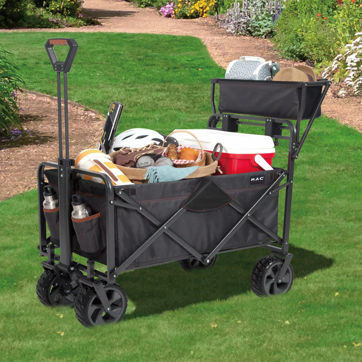 A heavy-duty black Mac Sports Deluxe Folding Wagon stands on a grassy field, highlighting its wide all-terrain wheels, integrated front brakes, and extended telescoping handle.