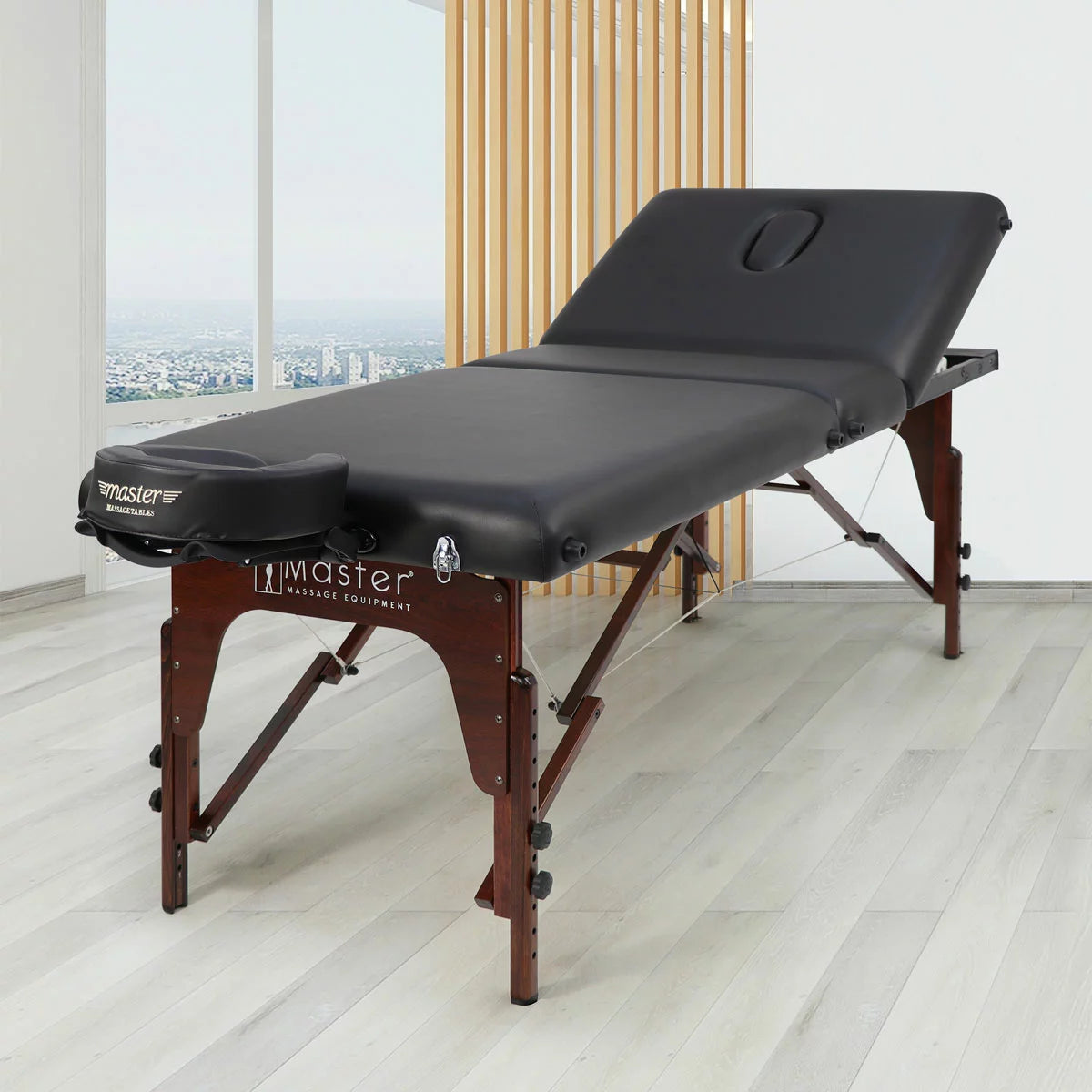 The Master Massage SomeRest table featuring its adjustable liftback in a raised position, displayed in a bright, modern studio with its included face cradle and carrying case nearby.