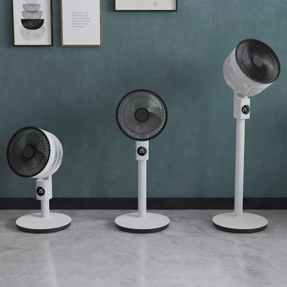 White Meaco Sefte 10 inch 3-in-1 pedestal air circulator standing on a light wood floor next to a modern sofa, showing its convertible height columns and sleek display head.