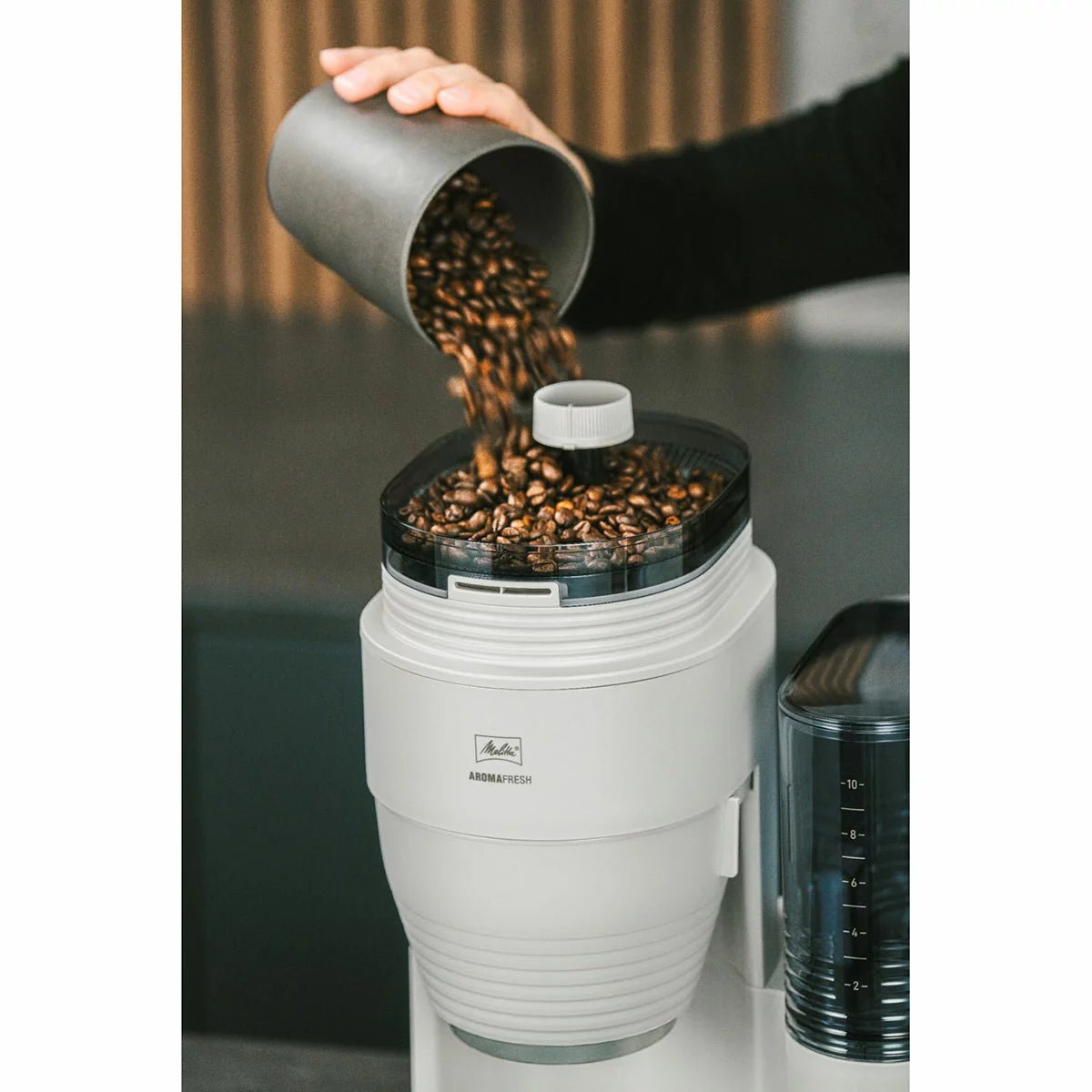 Side profile of the black and stainless steel Melitta AromaFresh Grind & Brew coffee machine with a glass carafe set on a clean kitchen countertop.