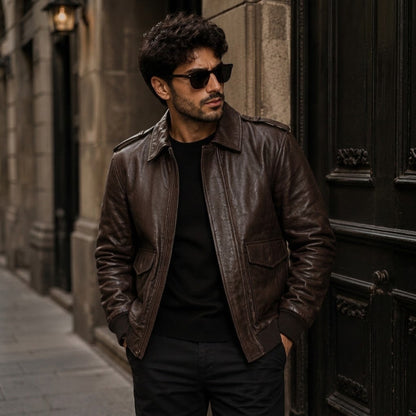 Men's vintage brown leather bomber jacket with ribbed cuffs and brass zipper shown on a wooden hanger against a dark backdrop.