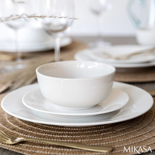 The Mikasa Alexis 12-Piece Porcelain Dinnerware Set neatly arranged on a table, highlighting its clean white finish and modern coupe-style plates and bowls.