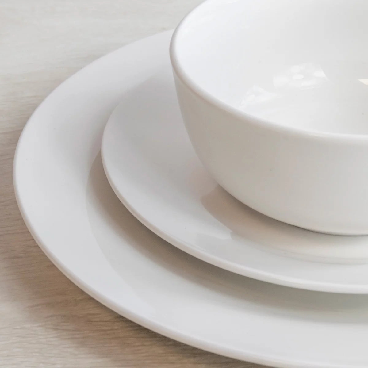 The Mikasa Alexis 12-Piece Porcelain Dinnerware Set neatly arranged on a table, highlighting its clean white finish and modern coupe-style plates and bowls.