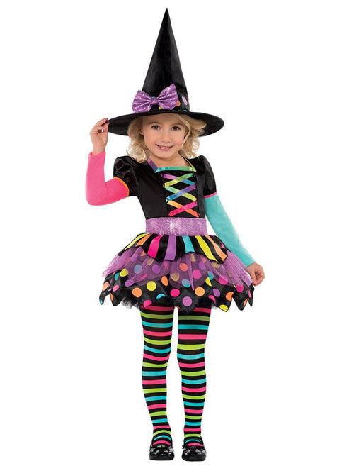 Toddler wearing the Miss Matched Witch costume featuring a vibrant neon striped dress and matching black witch hat on a hardwood floor setup.