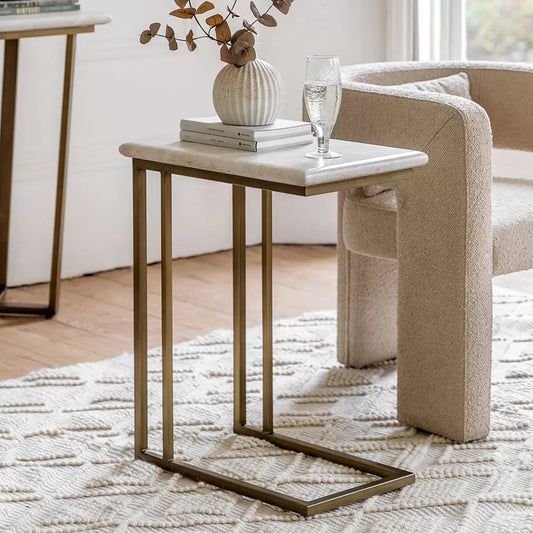 Cream-white faux travertine sofa table with a bronzed brass metal frame styled in a minimalist modern living room next to a neutral sofa.