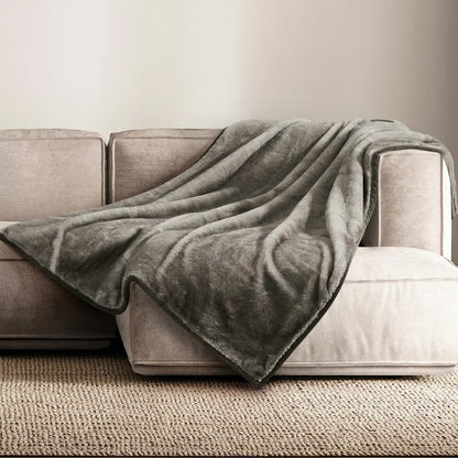 A plush grey Mon Chateau faux fur throw draped casually over the arm of a dark leather sofa in a cozy living room setup.