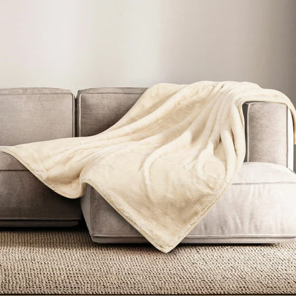 A plush grey Mon Chateau faux fur throw draped casually over the arm of a dark leather sofa in a cozy living room setup.