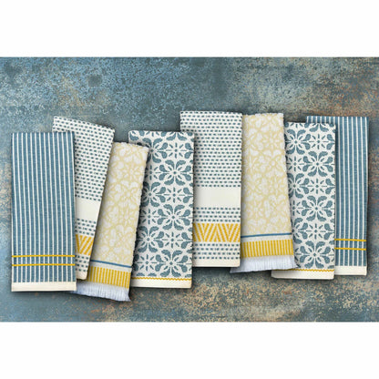 A stack of Mundo Textile kitchen towels in blue, red, neutral, and green patterns on a wooden kitchen surface.