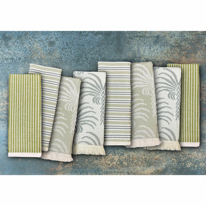 A stack of Mundo Textile kitchen towels in blue, red, neutral, and green patterns on a wooden kitchen surface.