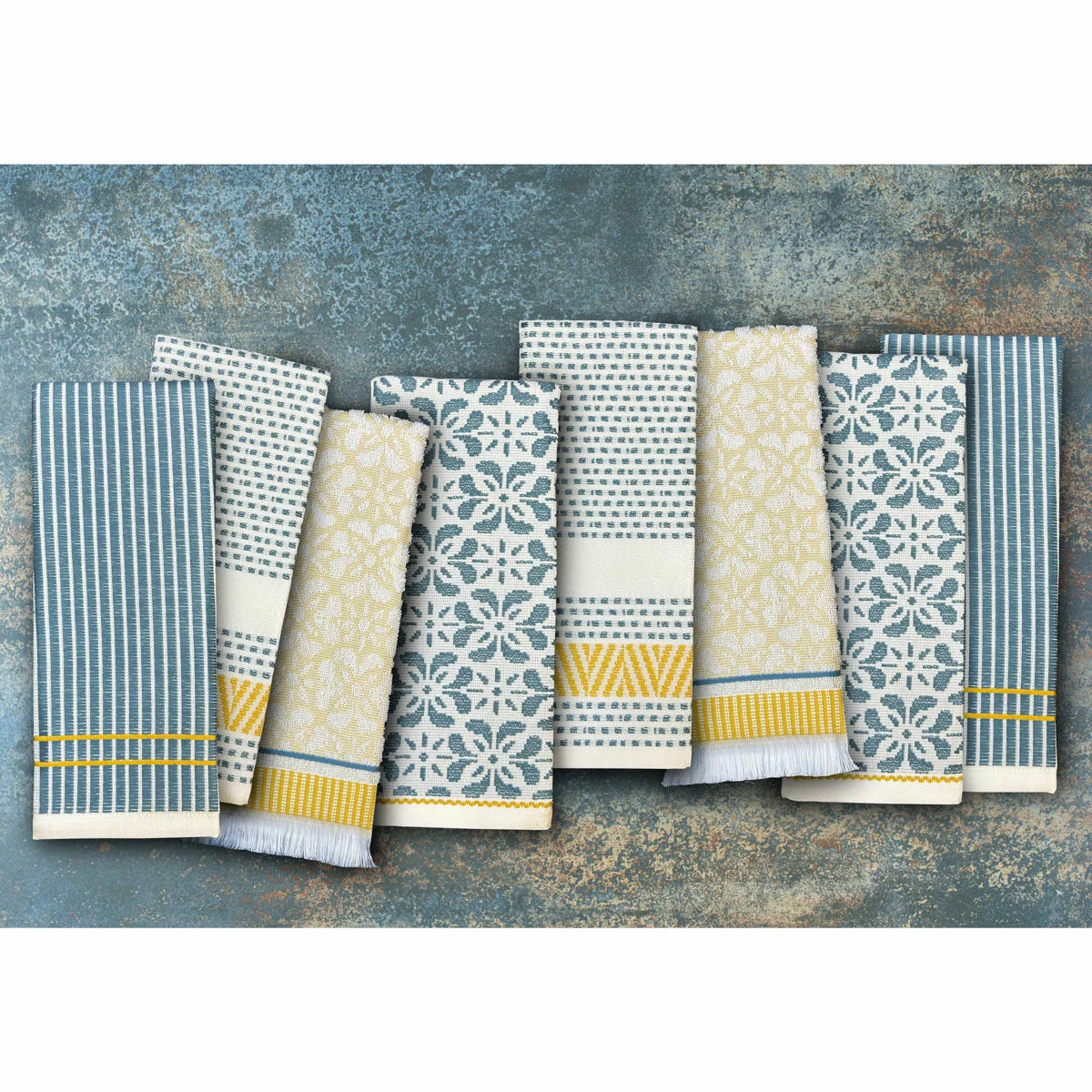 A stack of Mundo Textile kitchen towels in blue, red, neutral, and green patterns on a wooden kitchen surface.