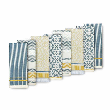 A stack of Mundo Textile kitchen towels in blue, red, neutral, and green patterns on a wooden kitchen surface.