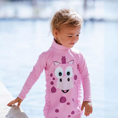 Toddler wearing bright orange My Little Swimsuit two-piece set with matching peaked hat on a sunny sandy beach setting.