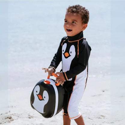 Toddler wearing bright orange My Little Swimsuit two-piece set with matching peaked hat on a sunny sandy beach setting.