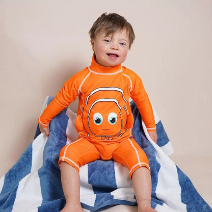 Toddler wearing bright orange My Little Swimsuit two-piece set with matching peaked hat on a sunny sandy beach setting.