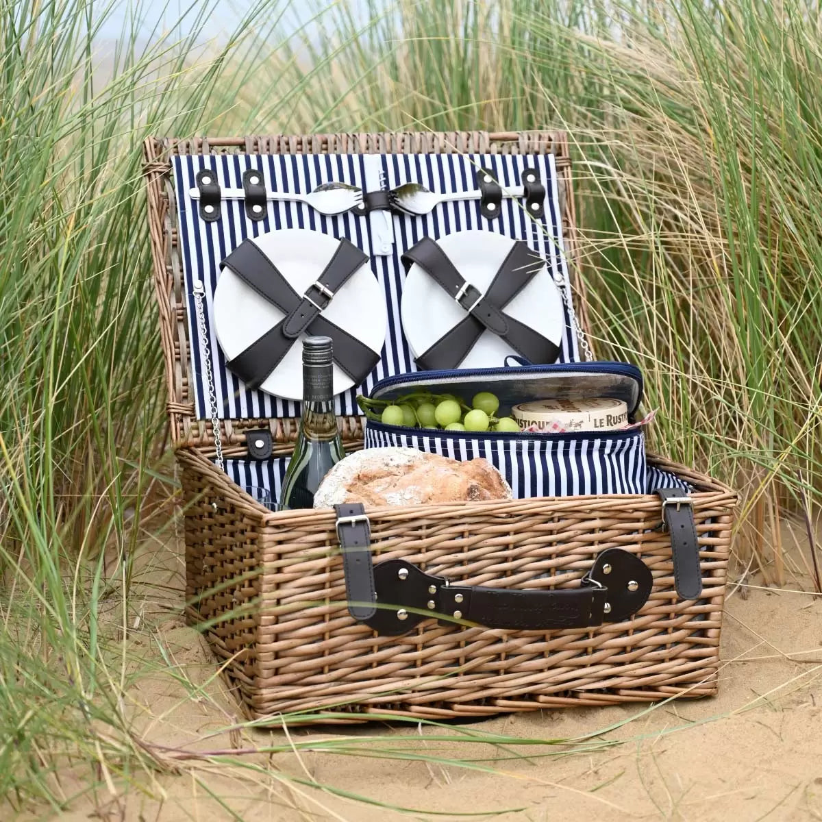 A traditional wicker Navigate 4 Person Picnic Basket opened to show fitted plates, cutlery, and an insulated interior.