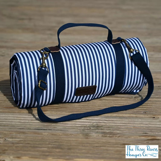 A navy and white striped Navigate Three Rivers picnic blanket spread out on green grass.
