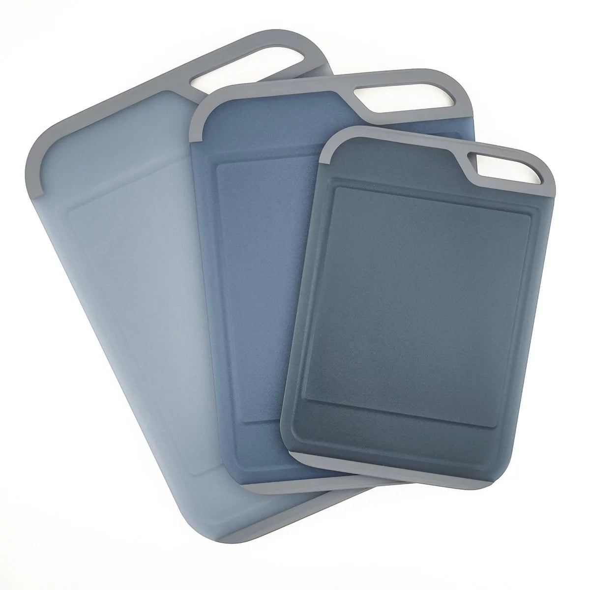 Three color-coded Neoflam cutting boards with non-slip handles and juice grooves stacked neatly on a white quartz kitchen countertop.