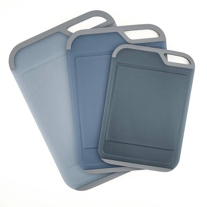 Three color-coded Neoflam cutting boards with non-slip handles and juice grooves stacked neatly on a white quartz kitchen countertop.