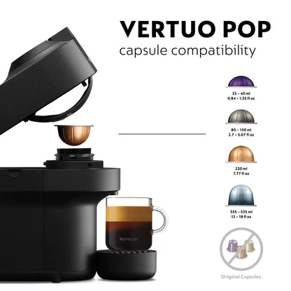 Front view of the matte black De'Longhi Nespresso Vertuo Pop coffee machine on a kitchen counter with a glass mug filled with layered coffee and rich foam.