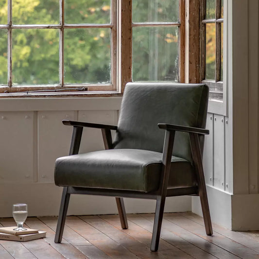 A high-angle close-up of the Gallery Neyland green leather armchair showing its textured top-grain leather seat and solid wood legs in a brightly lit, modern living room.