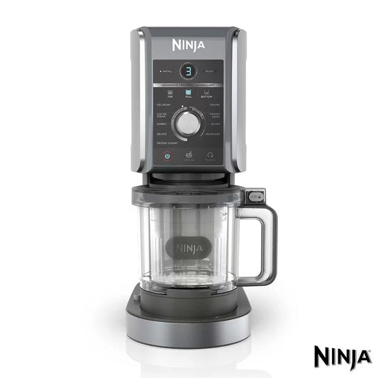 Front view of the matte silver Ninja CREAMi Deluxe NC501UK on a white kitchen counter next to a tub filled with fresh chocolate gelato and berries.