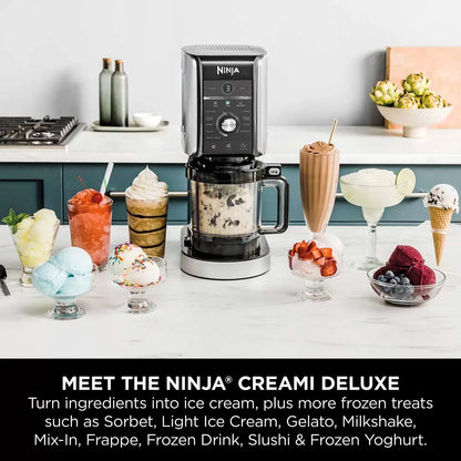 Front view of the matte silver Ninja CREAMi Deluxe NC501UK on a white kitchen counter next to a tub filled with fresh chocolate gelato and berries.