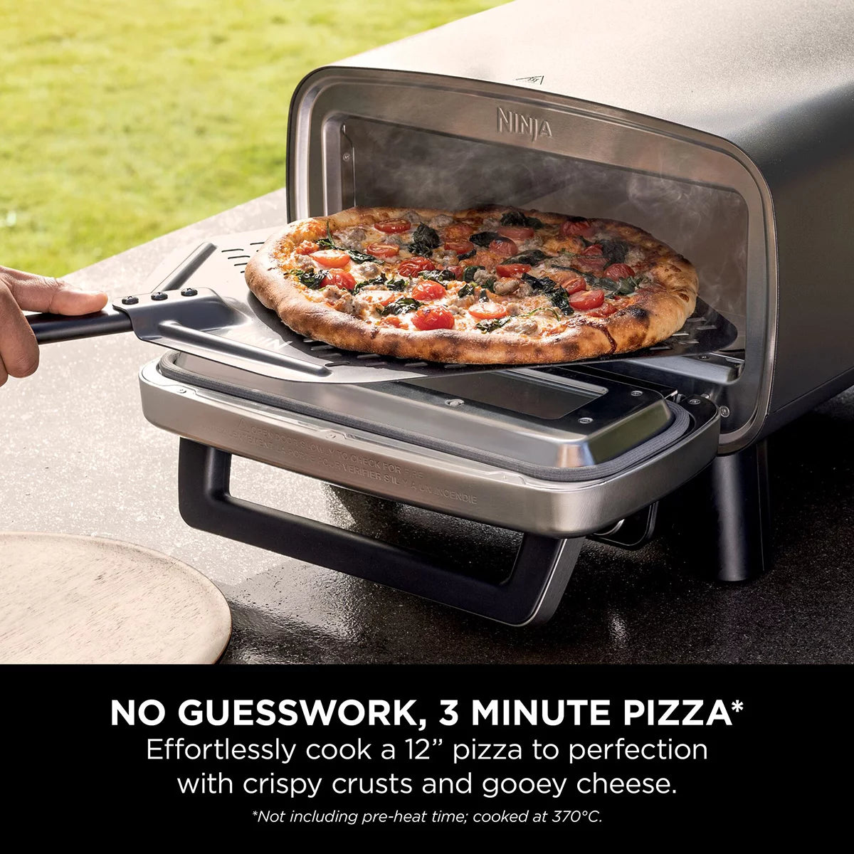 Front view of the grey Ninja MO203UK electric outdoor pizza oven with glowing interior light displaying a fresh 12-inch artisan pizza on the stone.