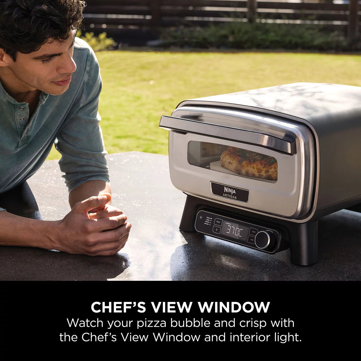 Front view of the grey Ninja MO203UK electric outdoor pizza oven with glowing interior light displaying a fresh 12-inch artisan pizza on the stone.