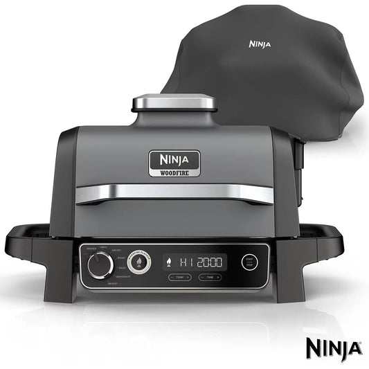 Front view of the grey Ninja OG703UK Woodfire Electric BBQ Grill & Smoker set up on a wooden outdoor patio counter with open lid revealing the grill plate.